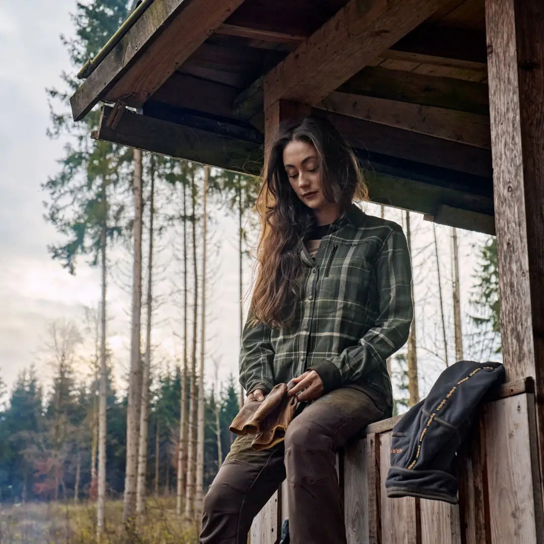 Woman in plaid shirt sitting outdoors, country clothing perfect for hunting and outdoor fun