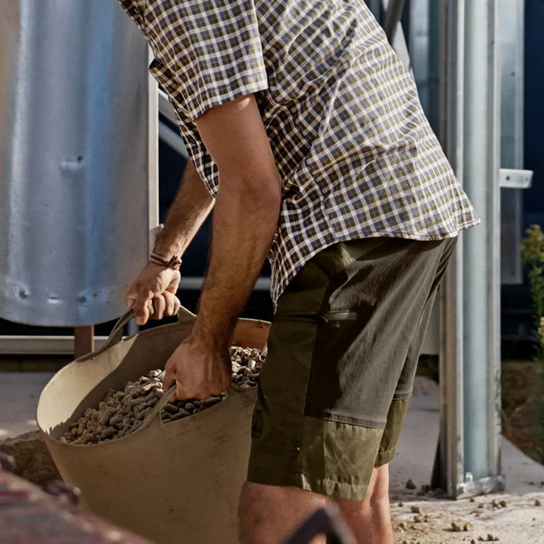 Man in Harkila Fjell Shorts carrying a bucket of pellets, perfect for country clothing and hunting
