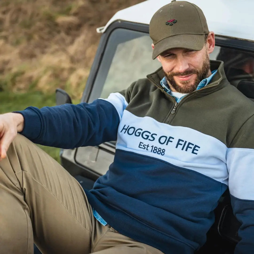 Man in a baseball cap and color-blocked jacket wearing a Hoggs Of Fife zip sweatshirt