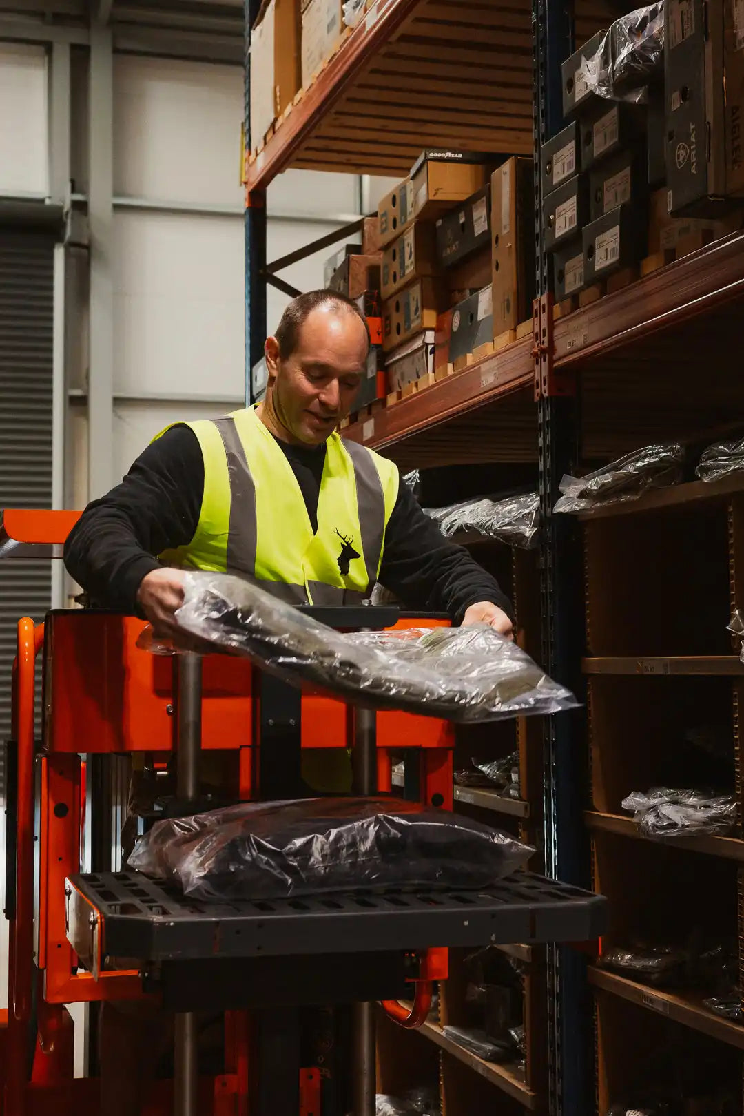 A male worker in a high-visibility vest handling packaged items in a warehouse.