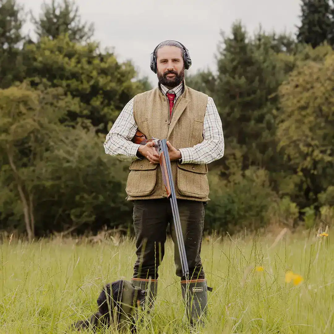 Man in hunting attire with shotgun showcasing a stylish Tweed Gilet for country clothing