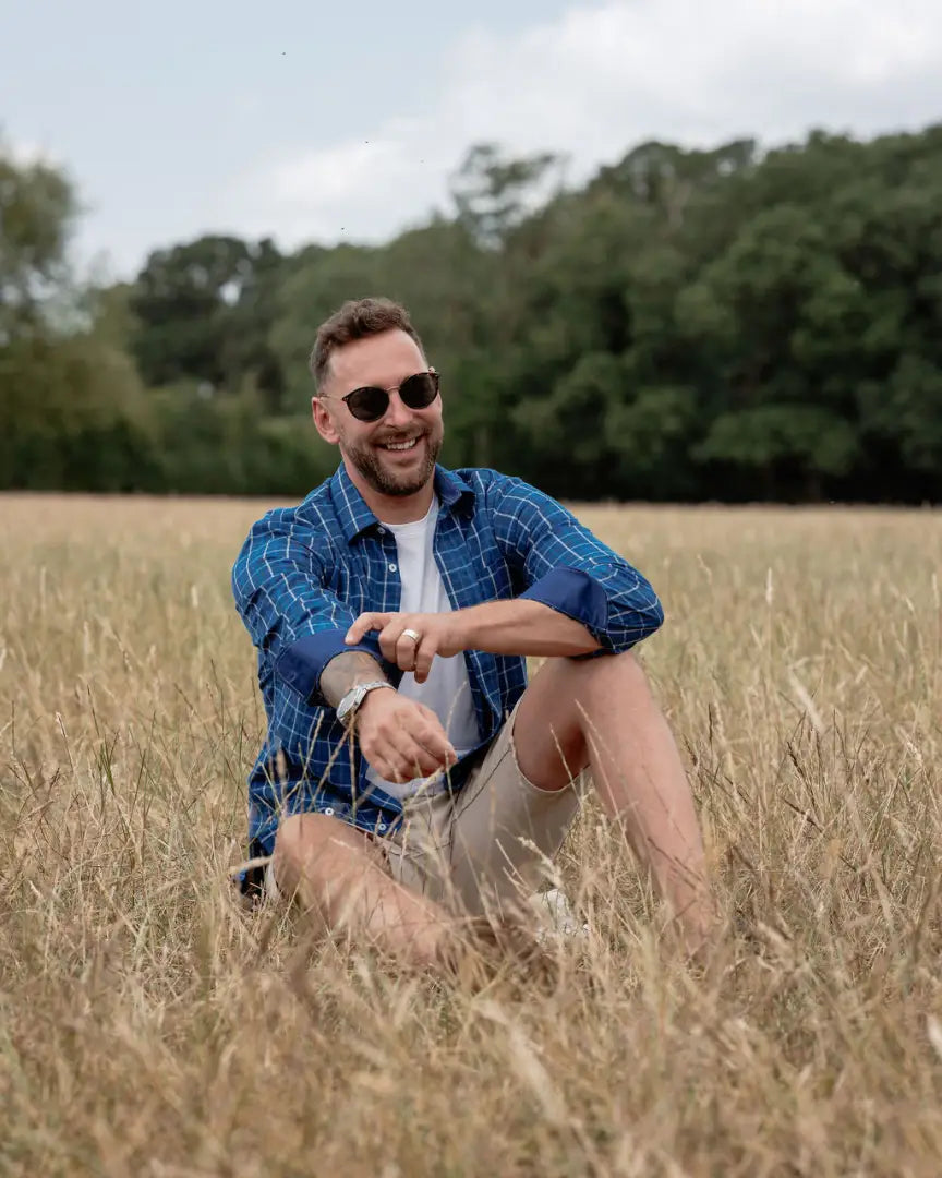 Man in sunglasses wearing forest premium tattersall shirt sitting in a field