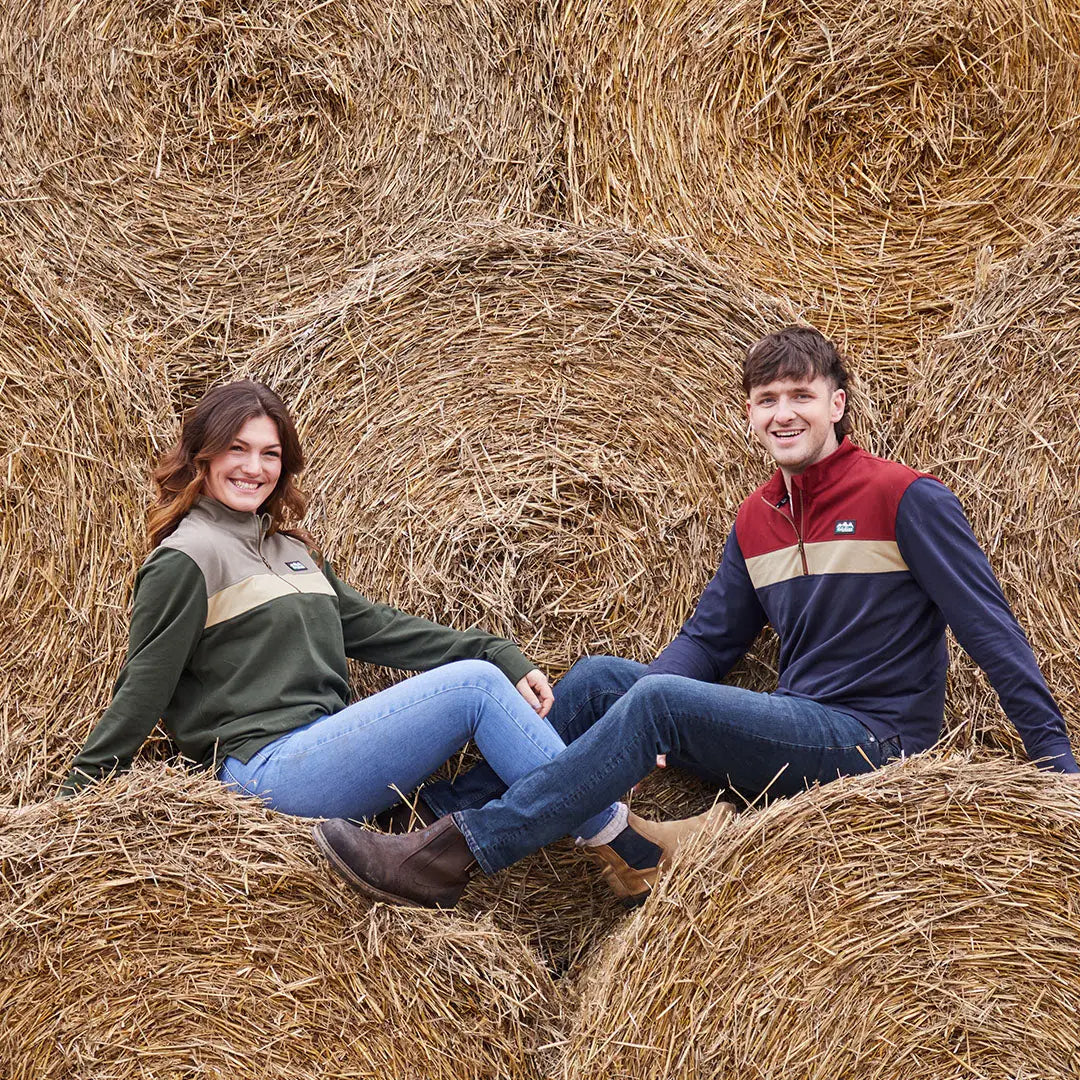 Two people in country clothing on hay bales wearing the Ridgeline Back Slider Rugby Top