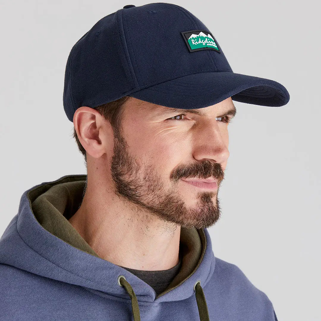 Man wearing Ridgeline Monsoon Classic Cap with green mountain logo and blue hoodie