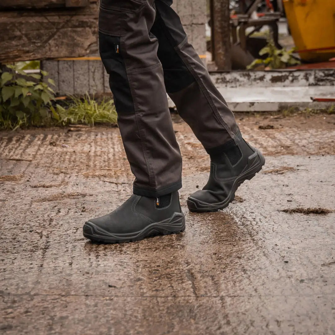 Person’s legs in dark work pants and black slip-on Xpert Defiant S3 Safety Dealer Boot