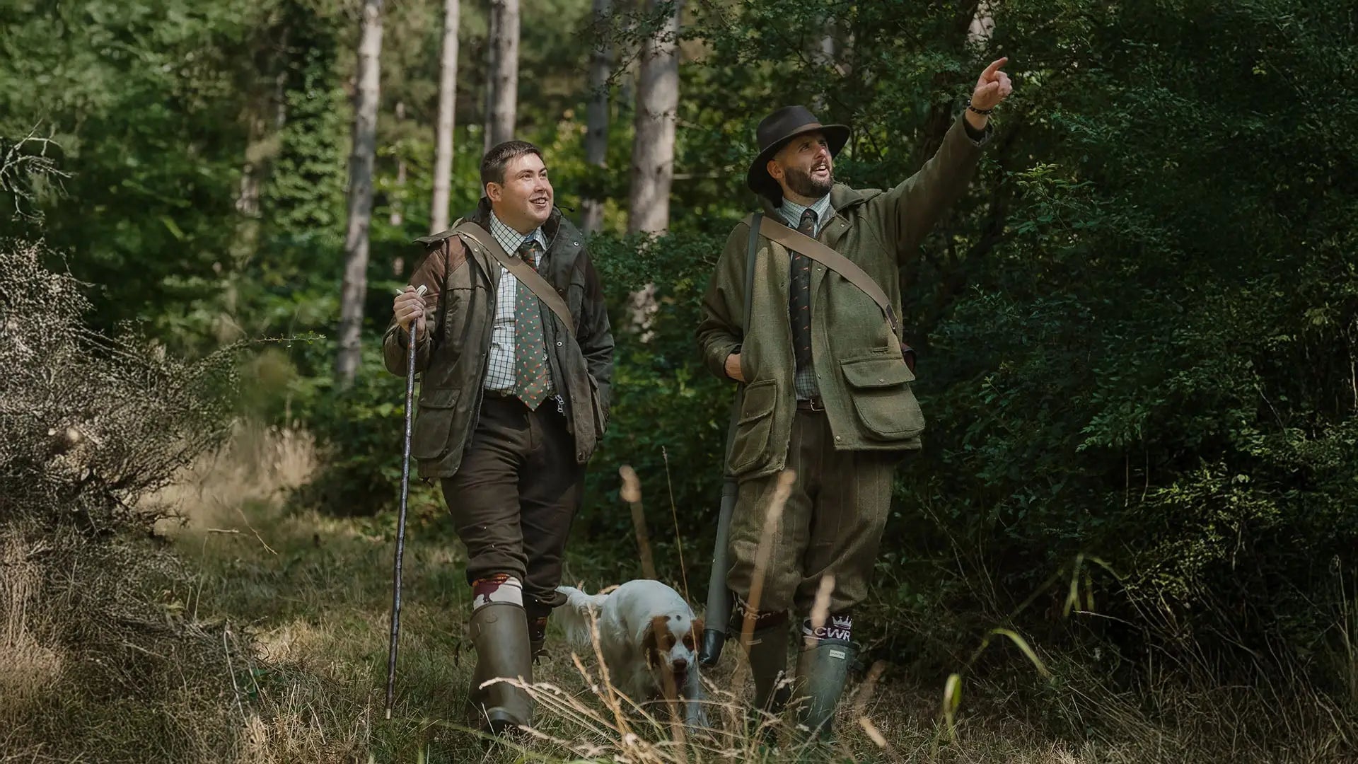 Two men in hunting attire with a dog in a forest for glorious twelfth country sport