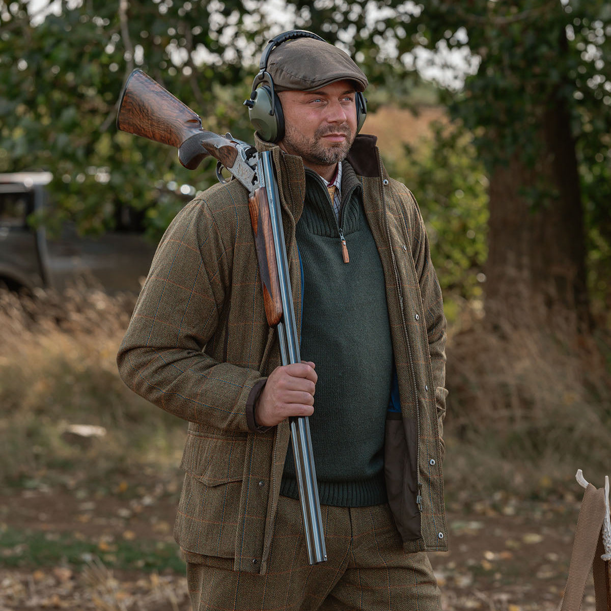 Man in hunting attire holding a shotgun in an outdoor setting