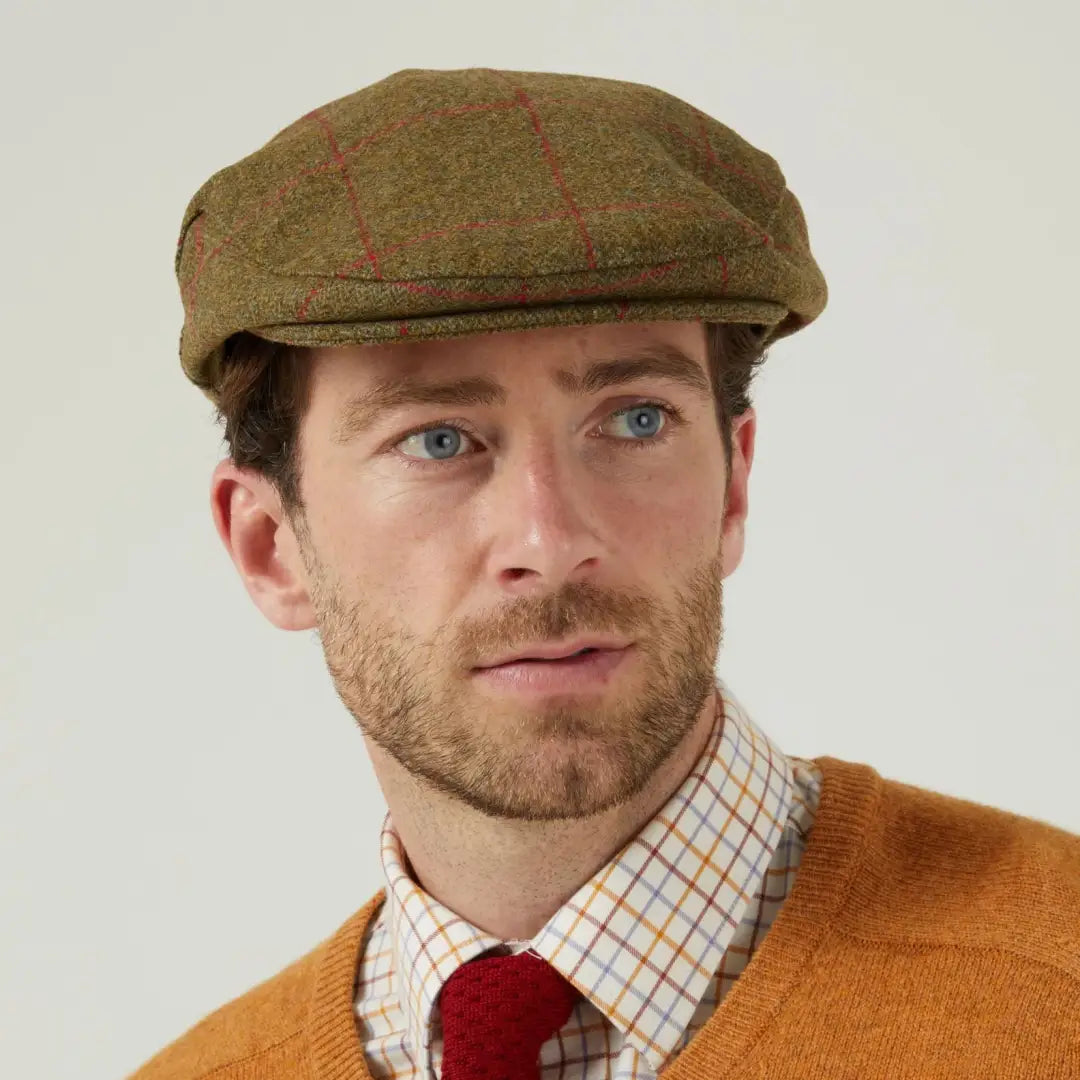 Man wearing Alan Paine Combrook tweed flat cap with plaid shirt and orange cardigan