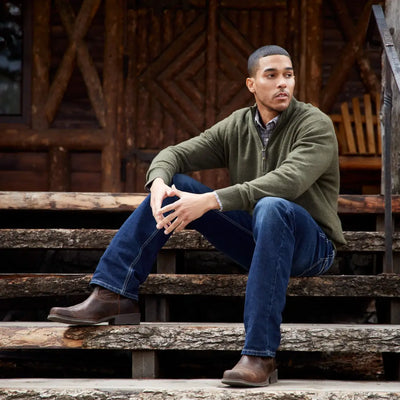 Man in green sweater and jeans on steps, showcasing Ariat Rambler Western Boots for outdoors