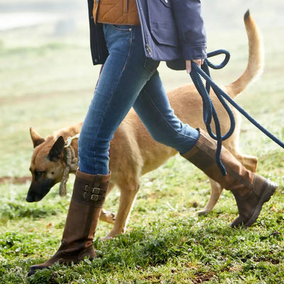 Dog on a leash with a person in jeans and Ariat tall waterproof boots for country outings