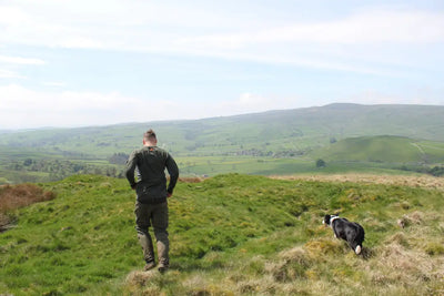 Man and dog on grassy hillside wearing Bushbuck Apex Crew Base Layer for outdoor comfort