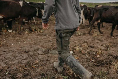 Person in muddy boots walking among cows wearing Bushbuck Venture Pants 2.0