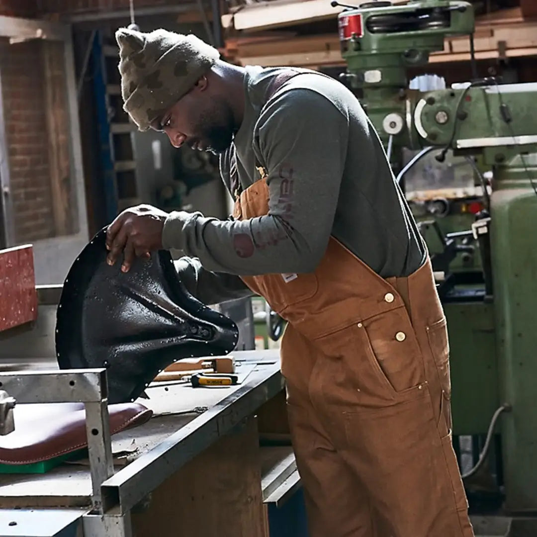 Man in brown Carhartt Relaxed Fit Duck Bib Overall inspecting outdoor country clothing for hunting