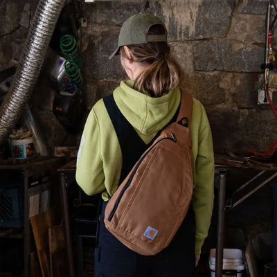 Tan Carhartt sling bag with canvas crossbody, black zipper, logo patch for outdoors hunting