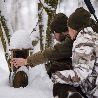 Snow-covered wooden birdhouse with a Deerhunter Cumberland Knitted Beanie nearby
