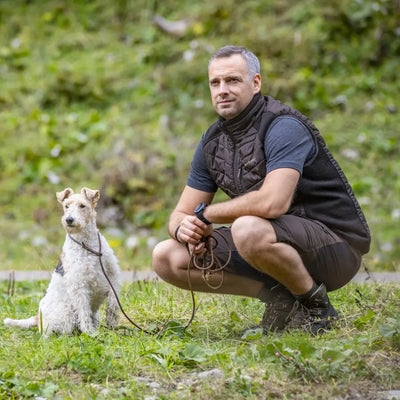 Man crouching with a small white dog in Deerhunter Moor Padded Waistcoat outdoors