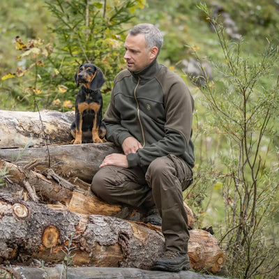 Man sitting with a dog on logs wearing Deerhunter Rogaland Trousers OEKO-TEX