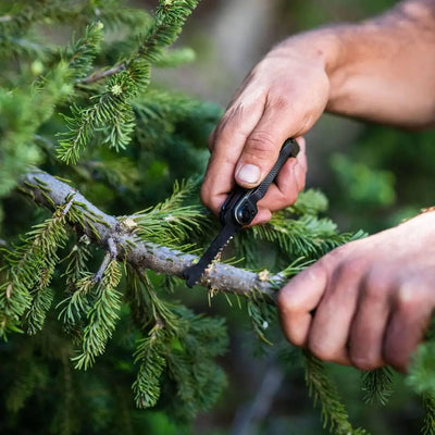Hands using Gerber Armbar Scout with stainless steel frame to trim an evergreen branch