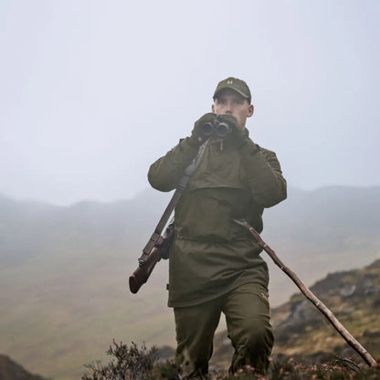 Hunter with binoculars and rifle wearing Härkila Orton Tech packable smock, ideal for country clothing