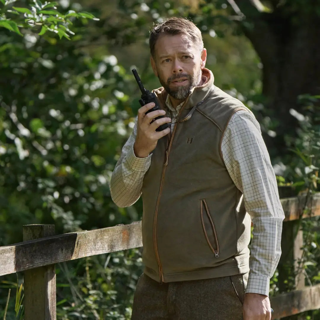 Man in olive vest holding walkie-talkie wearing Härkila Portfield Long Sleeve Shirt