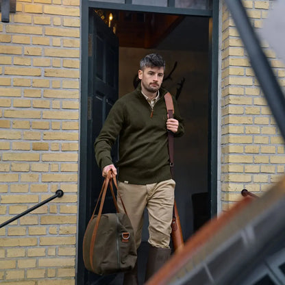 Man exiting doorway with duffel bag wearing Härkila Vincent Merino Half Zip Pullover