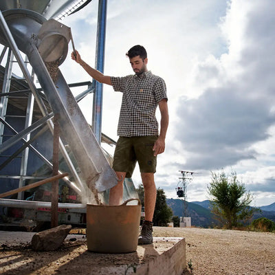 Man filling a bucket from a grain silo while wearing Harkila Fjell Shorts for hunting