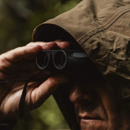 Hands holding Highlander Tarn 8X21 Binoculars in khaki sleeve, offering outstanding vision