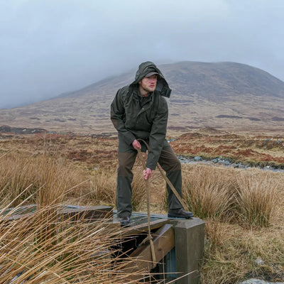 Person in a green hooded jacket on wooden structure, showing Fife Green King II Waterproof Trousers