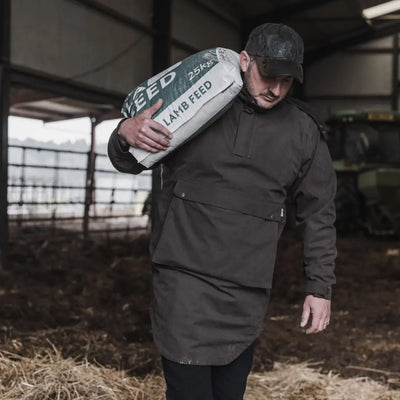 Man in longer length smock carrying lamb feed in a rustic barn setting
