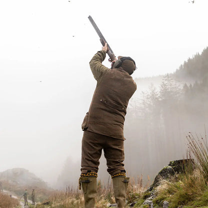 Hunter in Jack Pyke shooting vest aims shotgun in misty sky