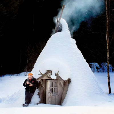 Snow-covered wooden hut with smoking chimney, perfect for country clothing and outdoors vibes
