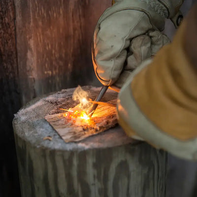 Gloved hands using a Kupilka Firesteel compact striker to ignite tinder outdoors