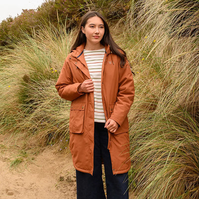 Young woman wearing Lighthouse Imogen Ladies Coat in rust over striped top and dark pants
