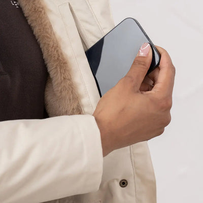 Person in a fur-lined Lighthouse Isobel Coat holding a smartphone outdoors
