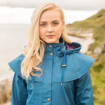Blonde woman in a teal Lighthouse Outback full length ladies waterproof raincoat outdoors