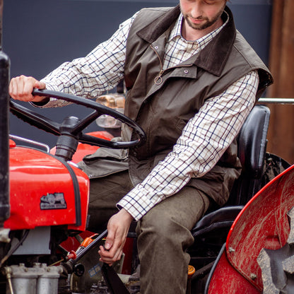 Man on a red tractor wearing a Forest Bushman Wax Gilet, ready for the outdoors