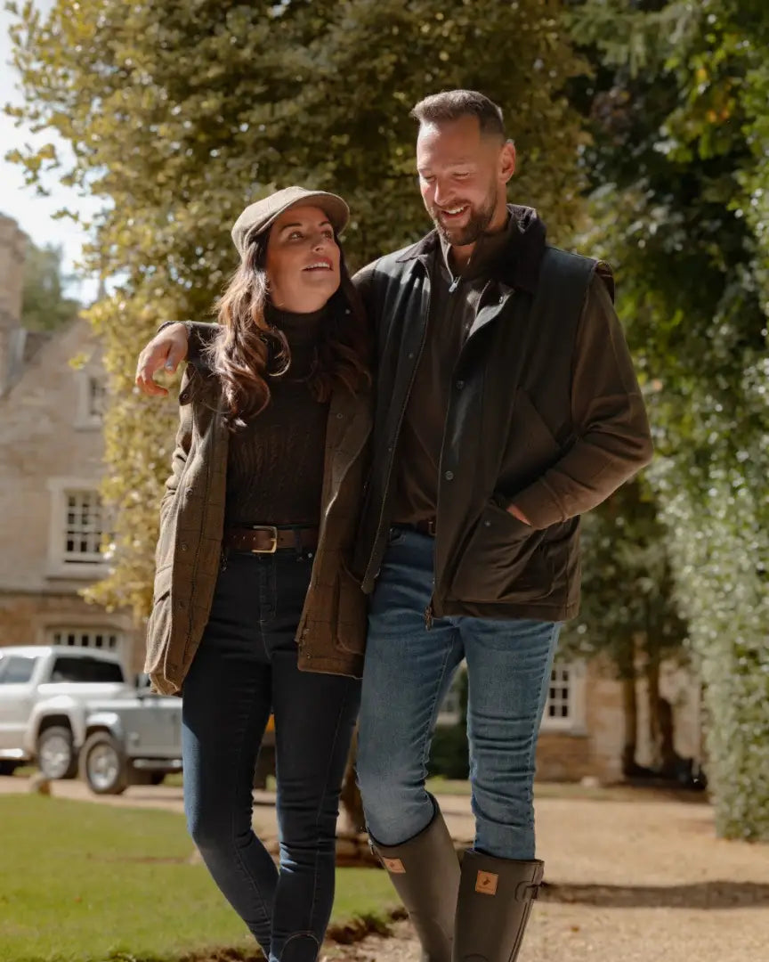 Smiling couple in casual forest bushman wax gilet, jackets, jeans, and boots
