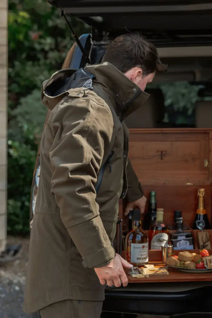 Person in olive green jacket pulling out a wooden box with bottles and food, perfect for forest country sport