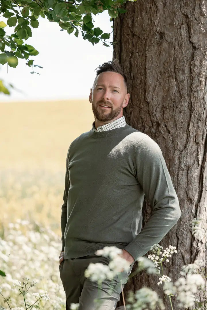 Man in green forest crew neck jumper leaning against tree outdoor style