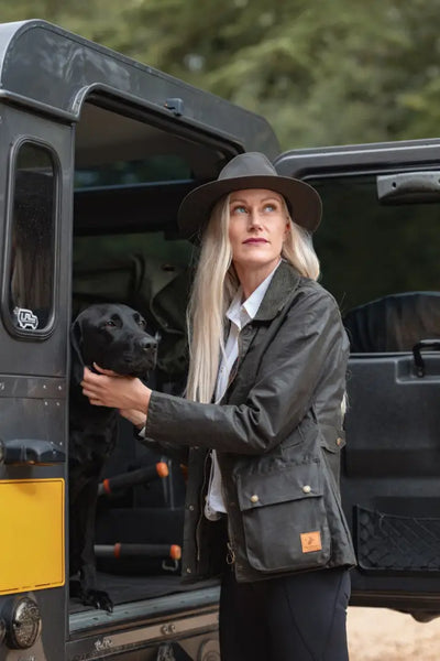 Woman in dark green Forest Harrison waxed jacket with black dog and wide brim Cupra Wax hat