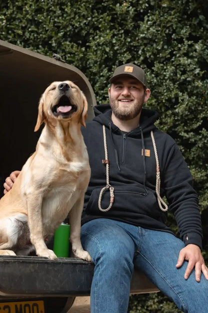 Man and dog relaxing on a truck bed wearing the New Forest Heathland Hoodie in forest heathland