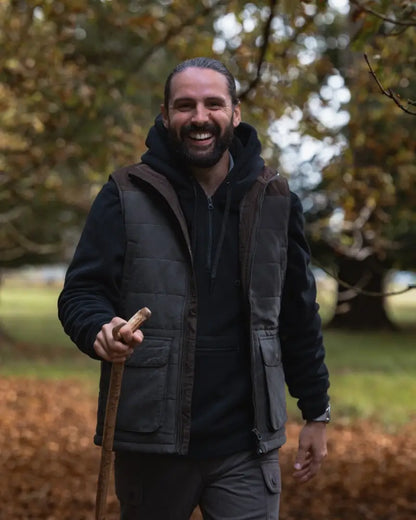 Smiling man with beard wearing forest heathland hoodie and holding a walking stick