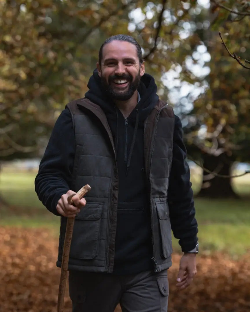 Smiling man with beard wearing forest heathland hoodie and holding a walking stick