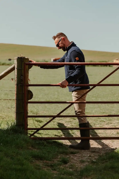 Man in outdoor clothing leaning on a metal gate wearing the Knightwood Quarter Zip Fleece