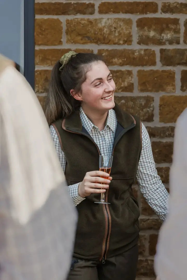 Young woman in fleece gilet holding champagne flute wearing New Forest Ladies Premium Tattersall Shirt