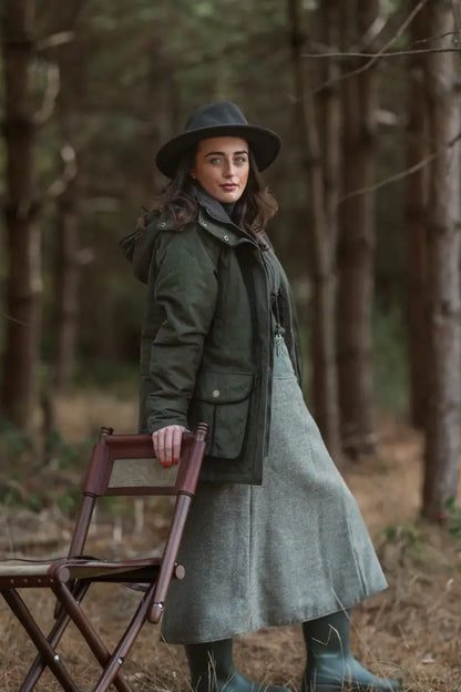 Woman in dark green Forest Ladies Robyn Jacket, light green skirt, and dark boots