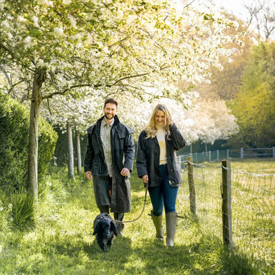 Couple in a traditional wax jacket walking a dog under blooming trees in the park