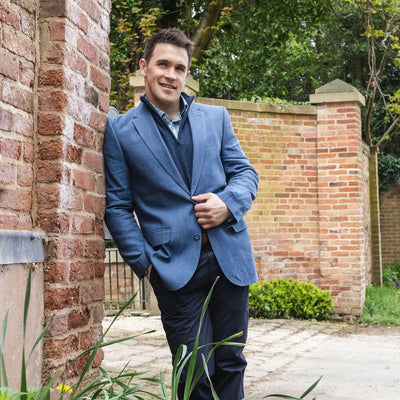 Man in a blue linen blazer next to a brick wall, perfect for country clothing and hunting