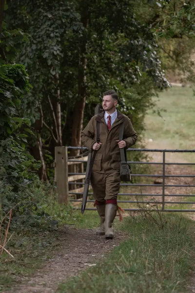 Man in hunting attire with shotgun and bag wearing the New Forest Maverick waterproof tweed jacket