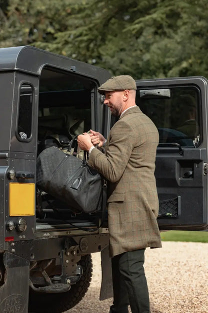 Man in tweed jacket and flat cap loading duffel into SUV wearing New Forest Moleskin Jeans
